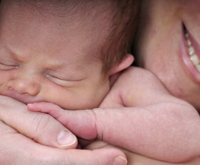 Newborn baby held close to the face of their smiling mother.