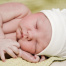 Sleeping newborn in a white hat, laying on their left side on a yellow green blanket